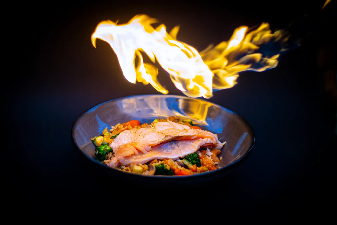 A plated wok dish with a burst of flame behind it
